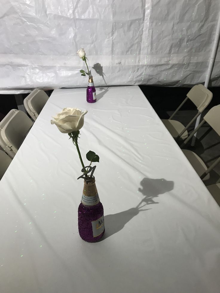 a white table topped with a vase filled with flowers next to a single white rose