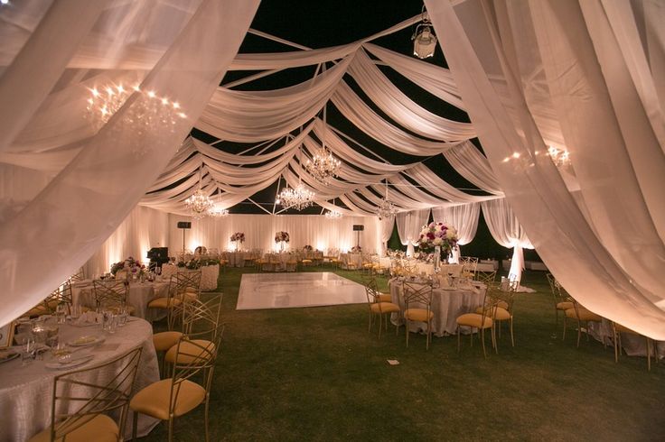 the inside of a tent with tables and chairs set up for a formal function at night