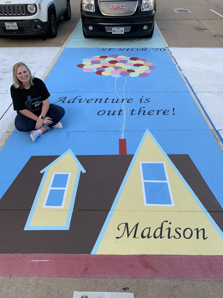 a woman sitting on the ground in front of a painted walkway with houses and balloons