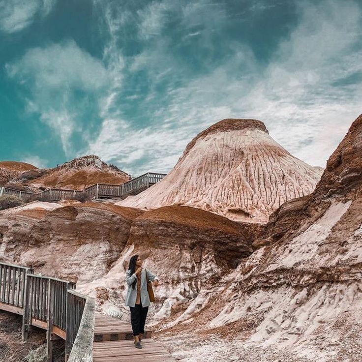 a woman walking down a wooden walkway in front of a mountain covered with white snow