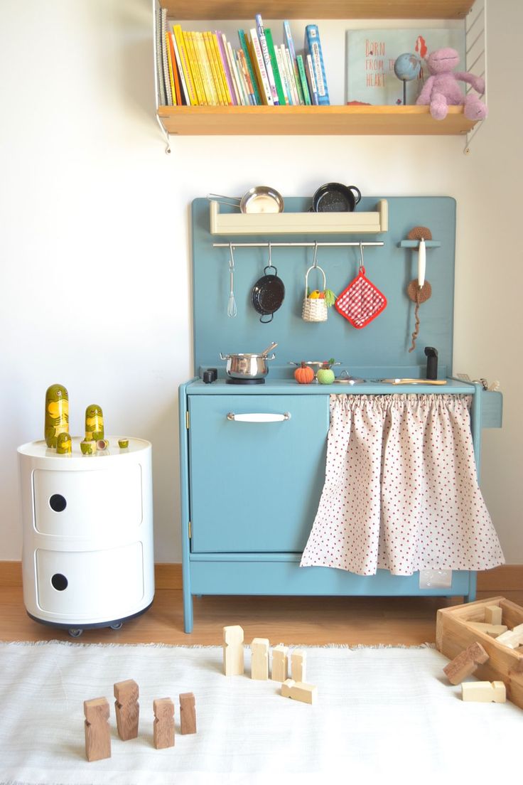 a blue stove top oven sitting inside of a kitchen next to a white rug and wooden toys