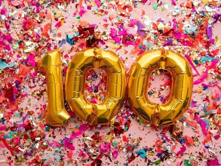 two balloons that are shaped like the number 100 on a table with confetti and streamers