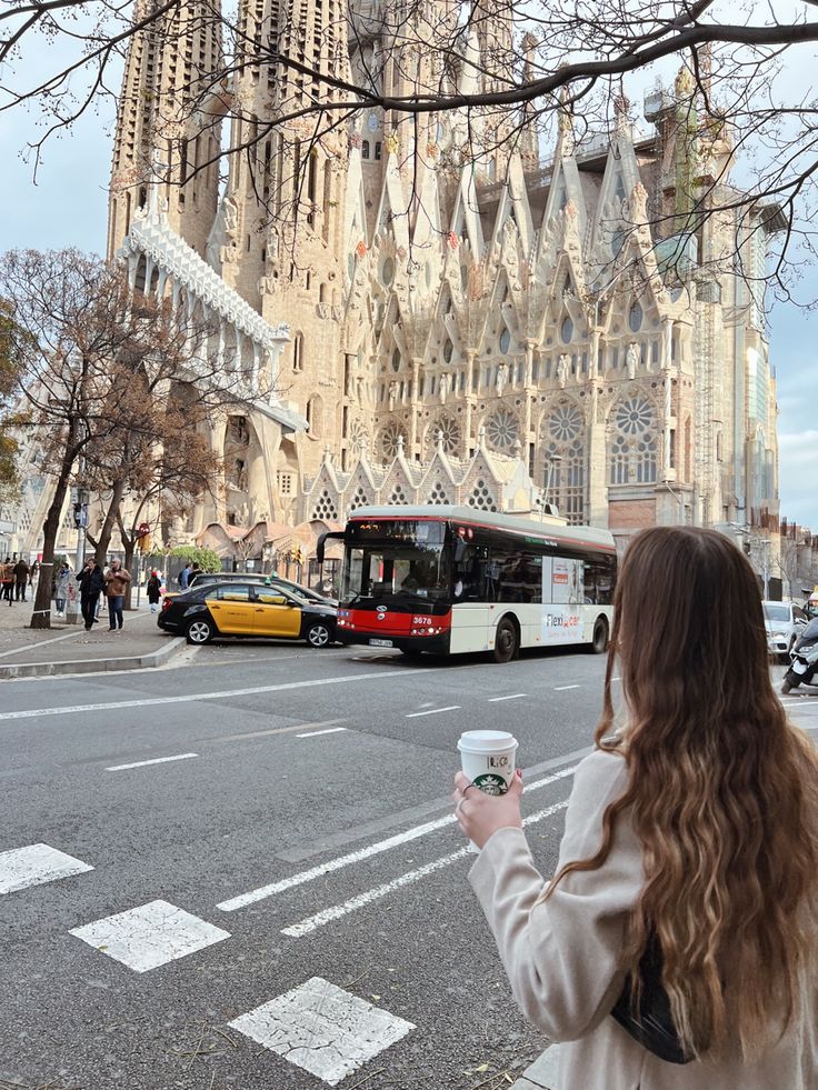 a woman standing on the side of a road holding a coffee cup in her hand