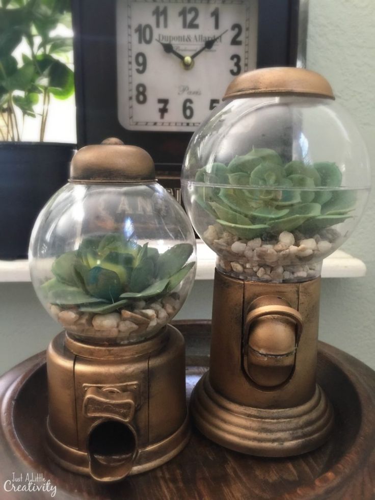 two glass balls with succulents in them sitting on a table next to a clock