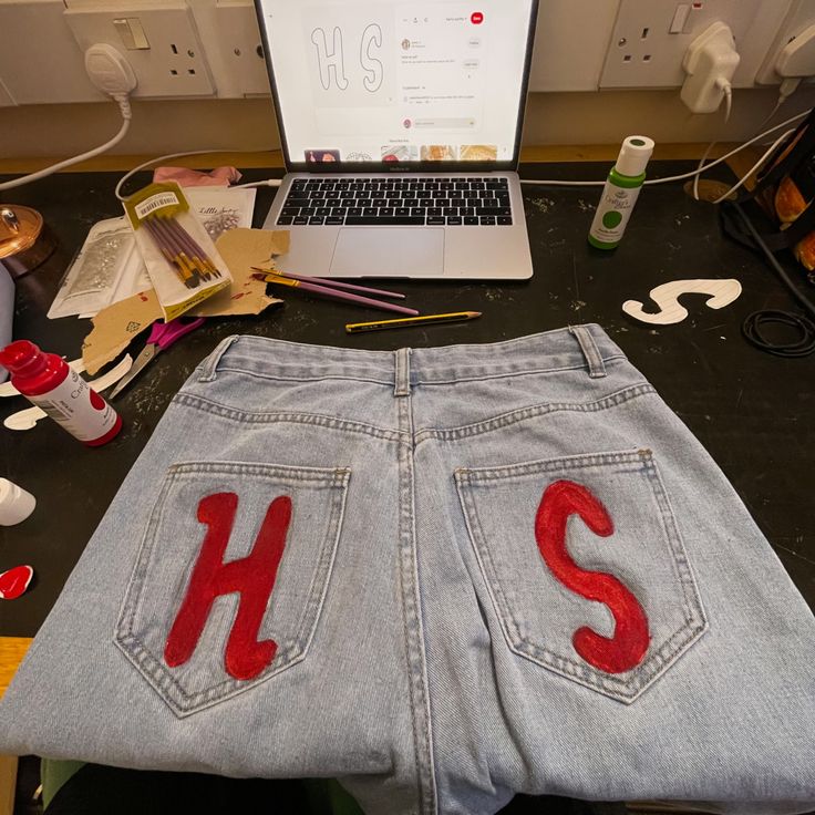 an open laptop computer sitting on top of a desk next to a pair of jeans