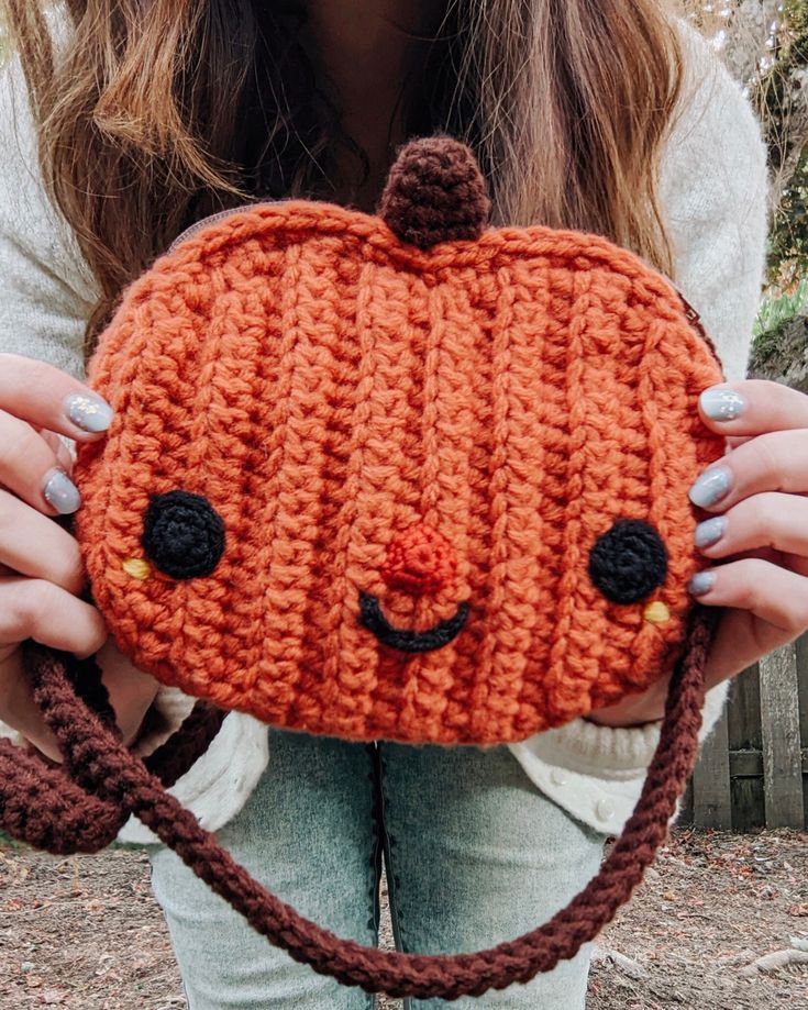 a woman holding an orange knitted pumpkin shaped purse with eyes and nose on it