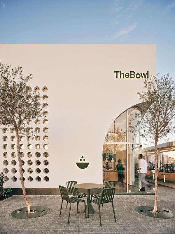 there is a table and chairs in front of the bowl building with people walking by