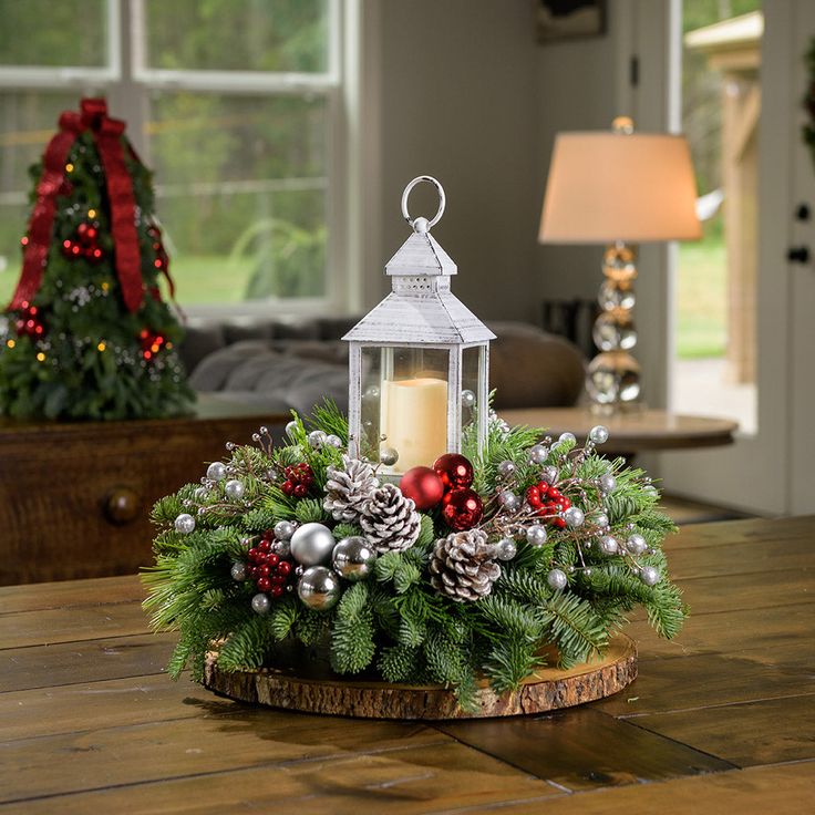 a christmas centerpiece with pine cones, ornaments and a lit candle on a wooden table