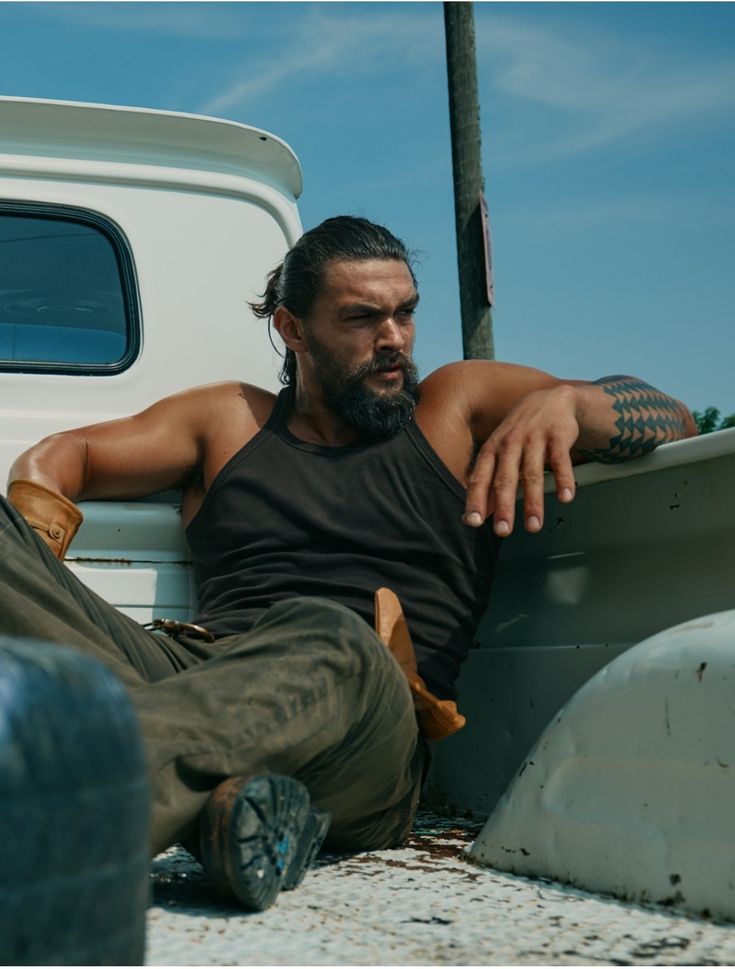 a man sitting on the ground next to a white truck with his foot up against it