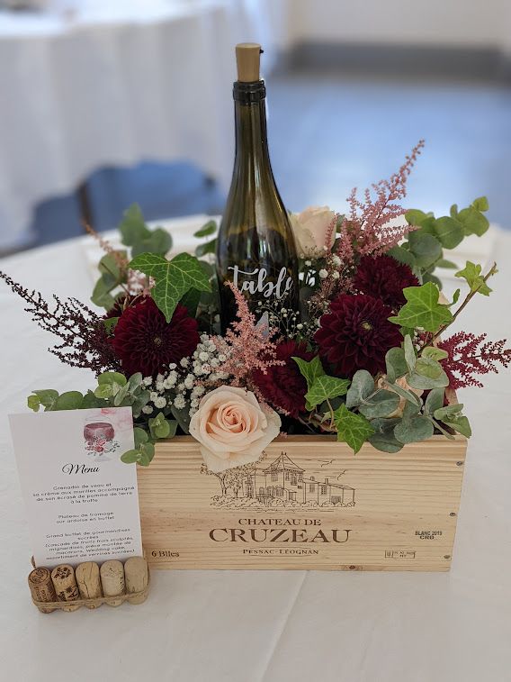 a bottle of wine sitting on top of a wooden crate filled with flowers and greenery