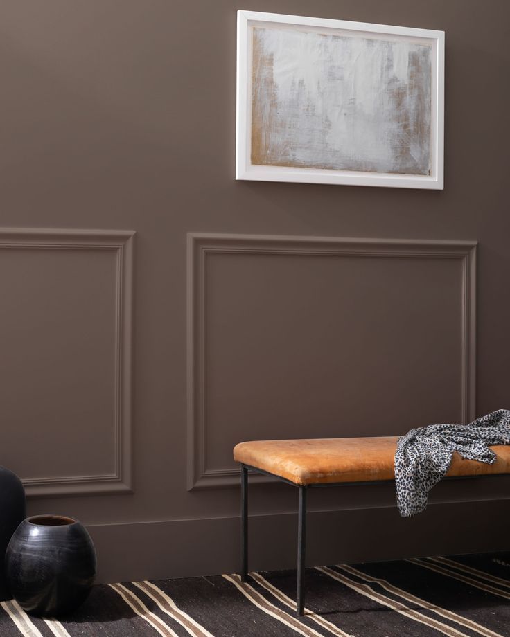 a wooden bench sitting in front of a wall with two black vases on it