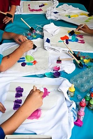 children are painting on t - shirts at a table with watercolors and crayons