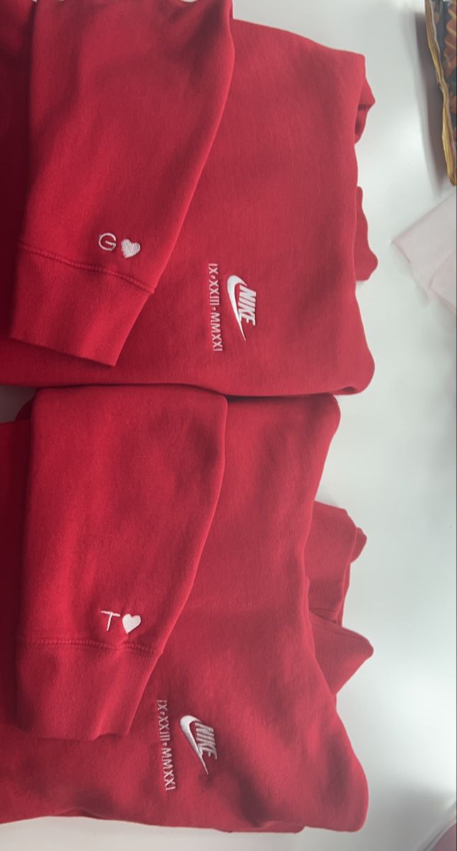 three red sweatshirts with hearts and arrows on them sitting on top of a table