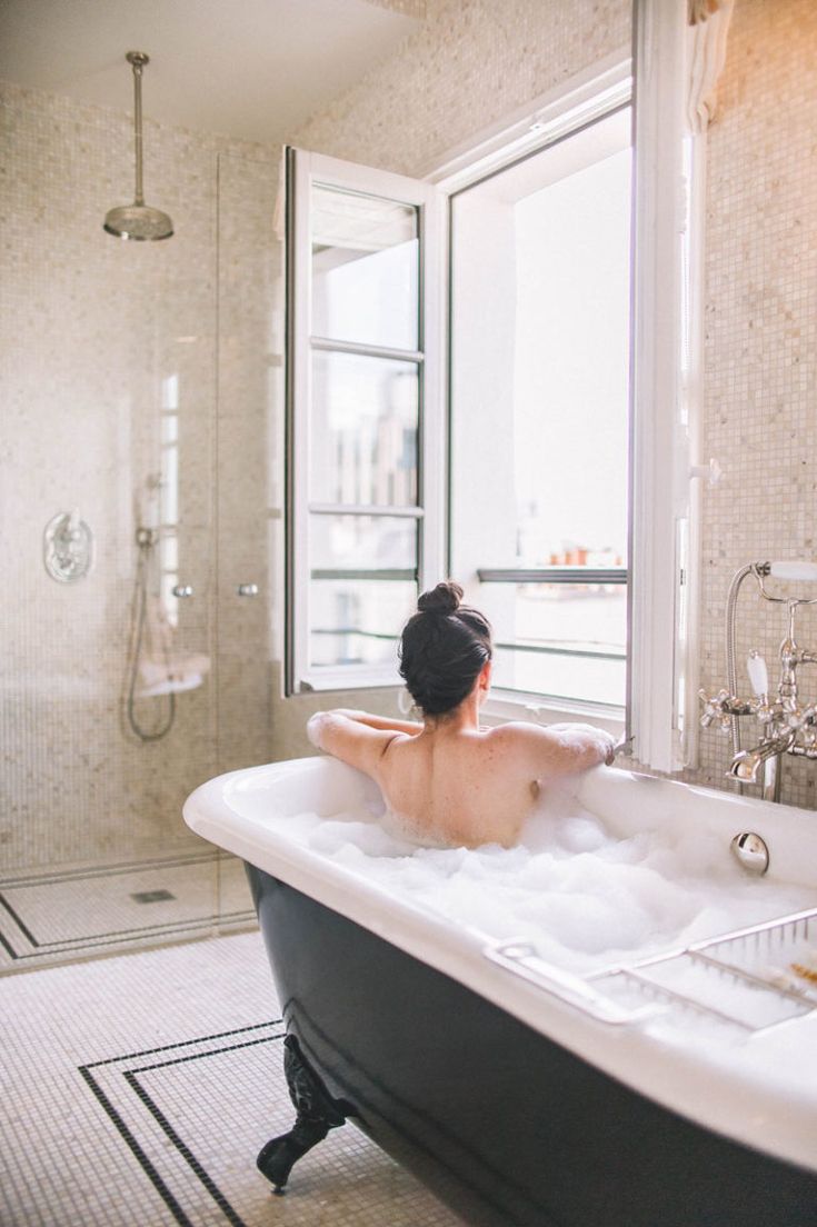 a woman sitting in a bathtub filled with foamy water next to a window