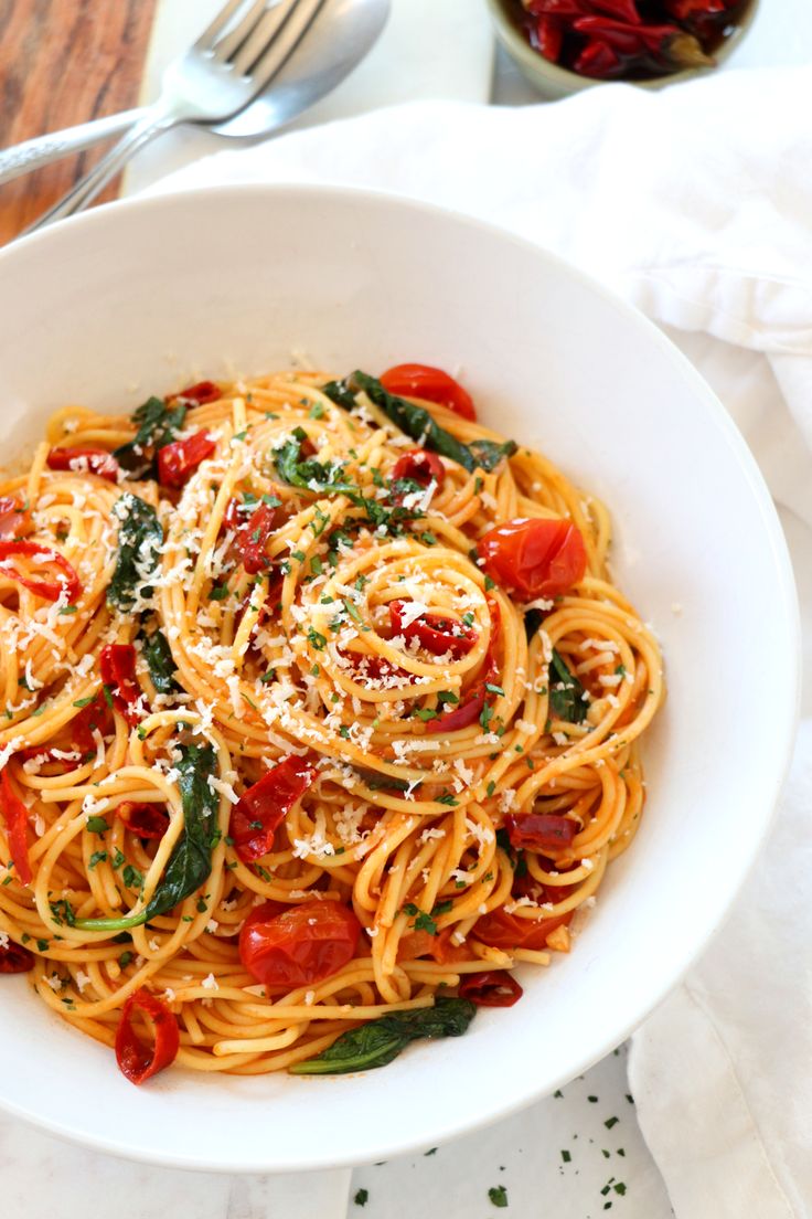 a white bowl filled with pasta and vegetables on top of a table next to silverware