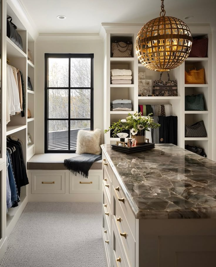 a walk - in closet with marble counter tops and white cabinets, along with an open window