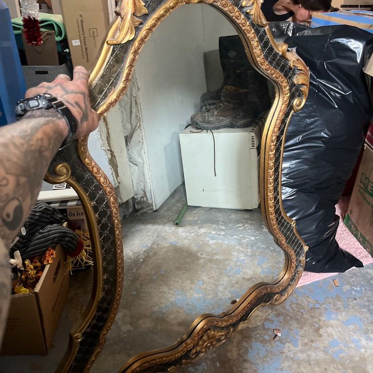 a man is looking at his reflection in a gold framed mirror that has been placed on the floor