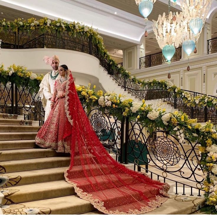 two people are standing on the stairs in front of some flowers and chandeliers