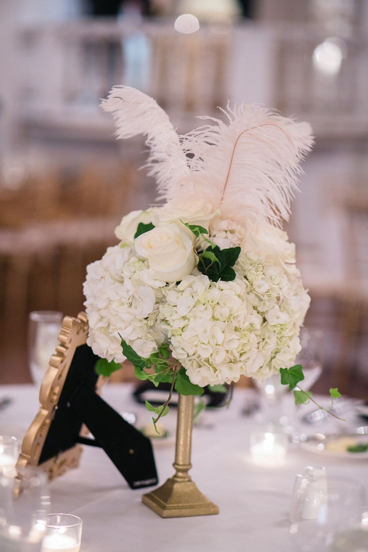 a centerpiece with white flowers and feathers is on a table at a wedding reception