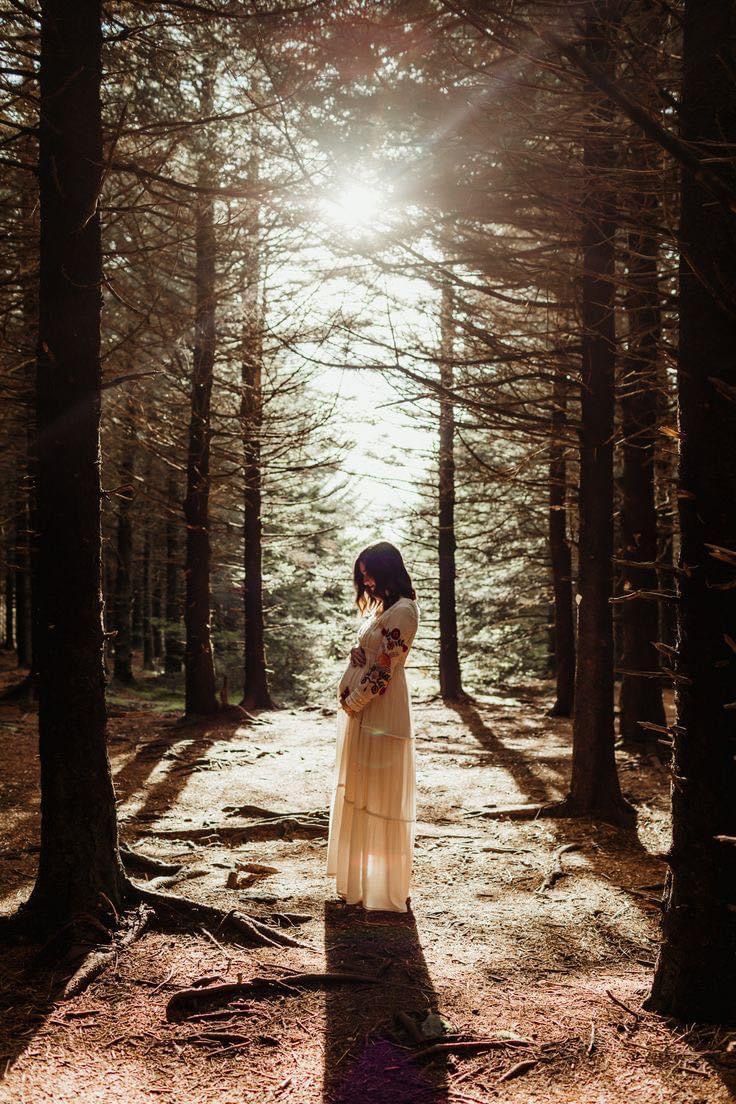 a woman standing in the middle of a forest with her hands on her chest and looking up