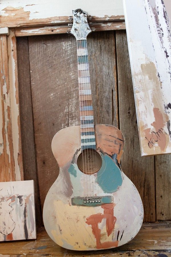 an old guitar sitting on top of a wooden table next to a wall with peeling paint