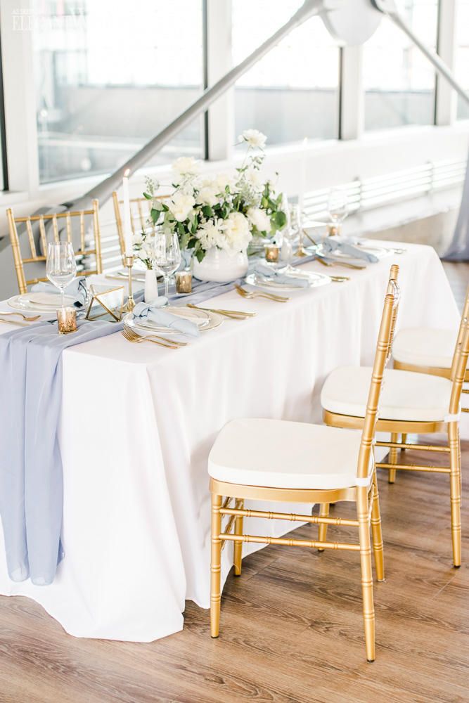 the table is set with white and blue linens, gold chairs, and flowers