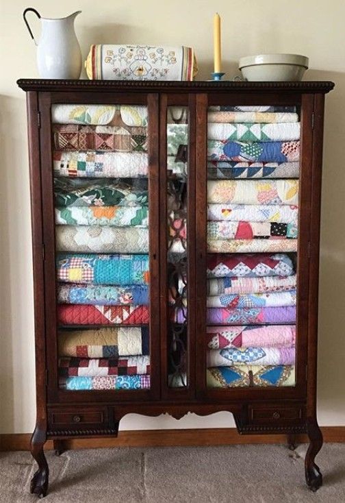 a cabinet with many quilts in it and a vase sitting on top of it