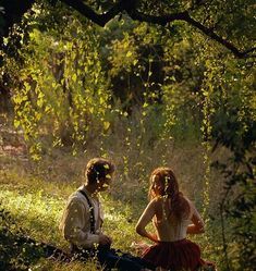 two people sitting on a log in the woods, one is talking to the other