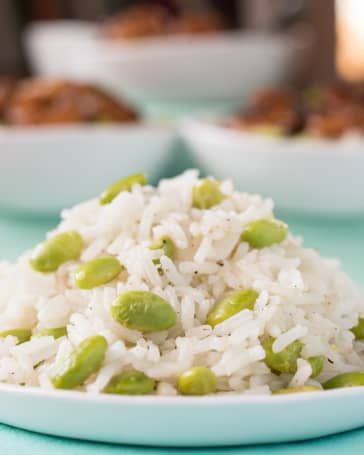 white rice with peas and pistachios on a blue tablecloth next to bowls of other food