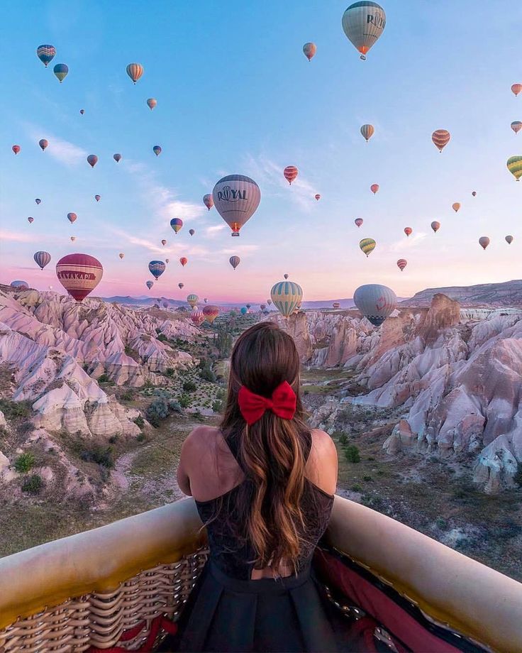 a woman sitting on top of a balcony looking at hot air balloons in the sky