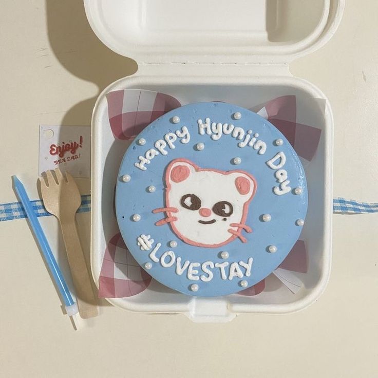 a plastic lunch box with a cat design on the lid and utensils next to it