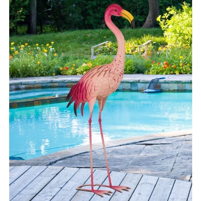 a pink flamingo standing on top of a wooden deck next to a swimming pool