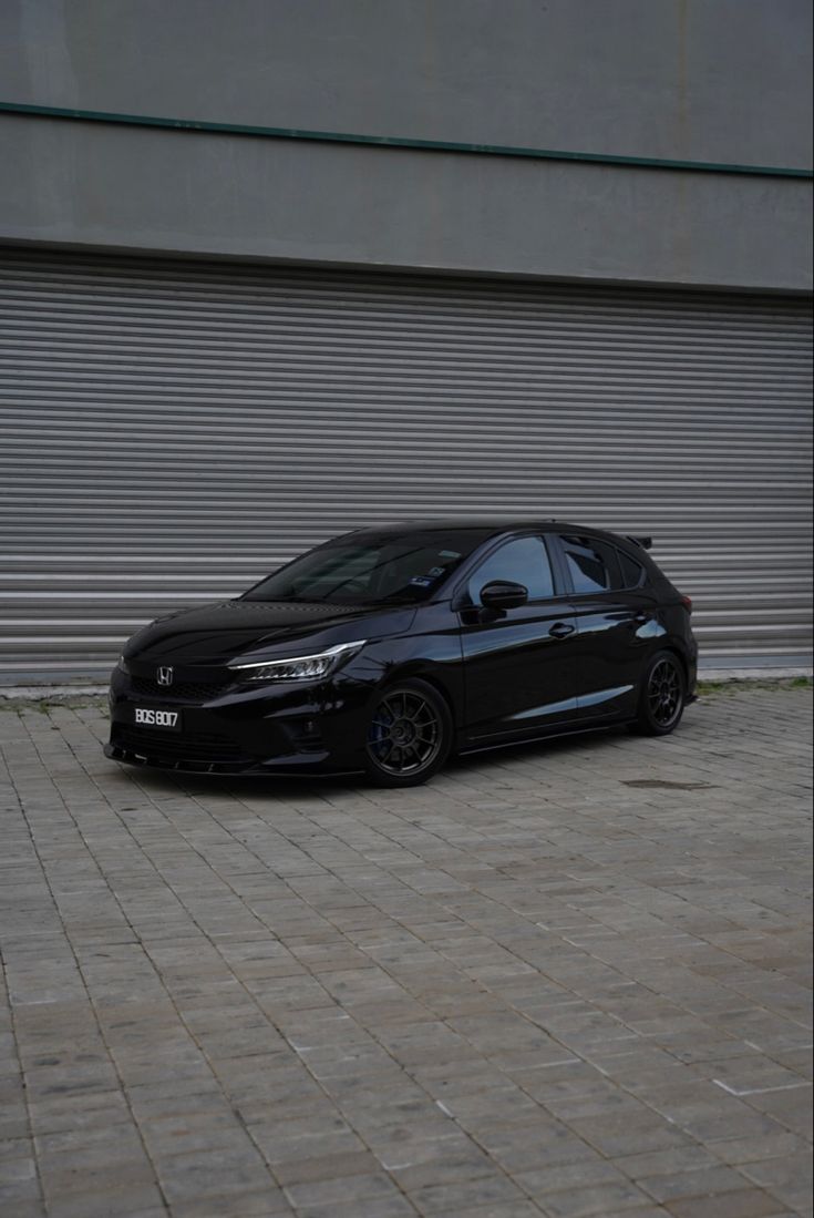 a black car parked in front of a garage door on a brick sidewalk next to a building