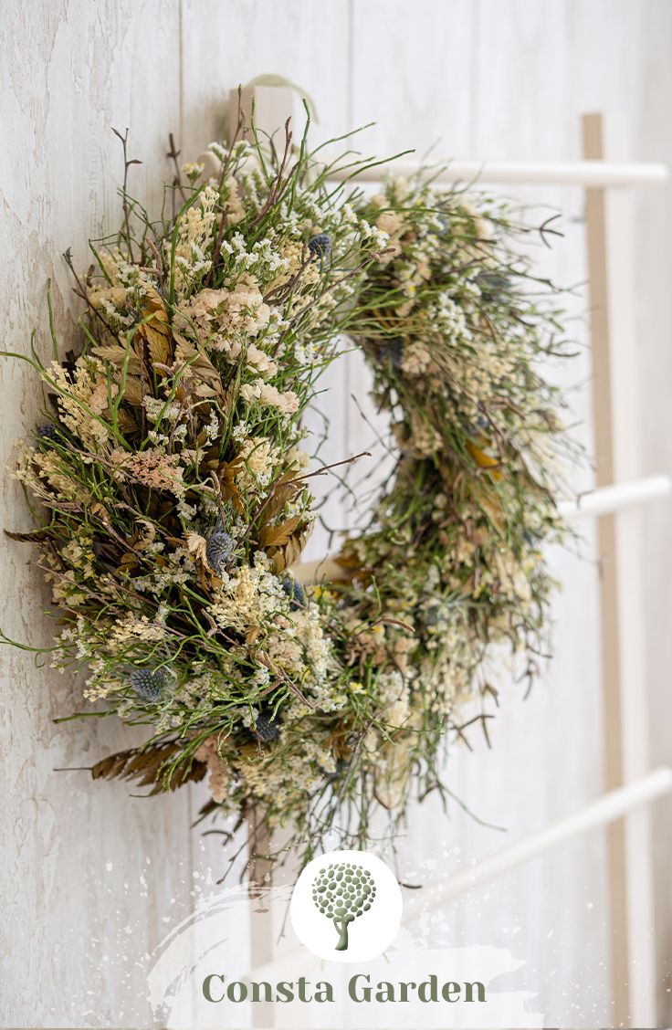 a wreath hanging on the side of a white wall next to a wooden ladder with a sign that says consta garden