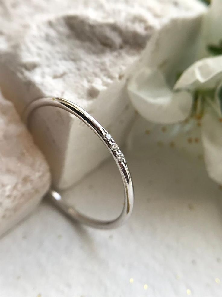 a close up of a wedding ring on a white surface with flowers in the background