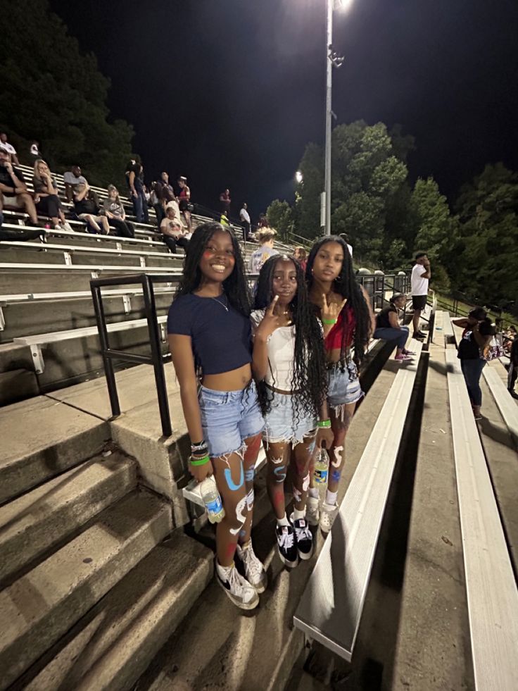 three girls are standing on the bleachers at night