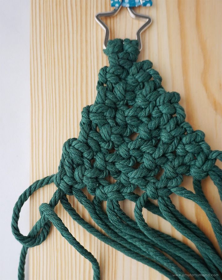 a green crochet piece with two metal hooks attached to it on a wooden surface