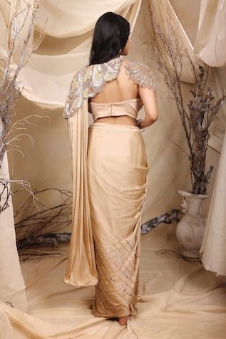 Golden beige pre-draped saree crafted in italian satin with nalki embellishments on the borders and sequin ray work on the bottom. Paired with a noodle strap sleeves cutwork border padded bustier with flora embroidery using cutdana, sequin, crystal and pearl highlights and an asymmetric sleeves cutwork border matching embroidered short shoulder cape. - Aza Fashions Pre-draped Saree With Mirror Work For Reception, Noodle Strap, Shoulder Cape, Drape Saree, Embroidered Shorts, Cut Work, Aza Fashion, Satin, Saree