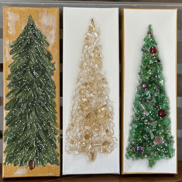 three small christmas trees are on display in their boxes, one is green and the other is gold