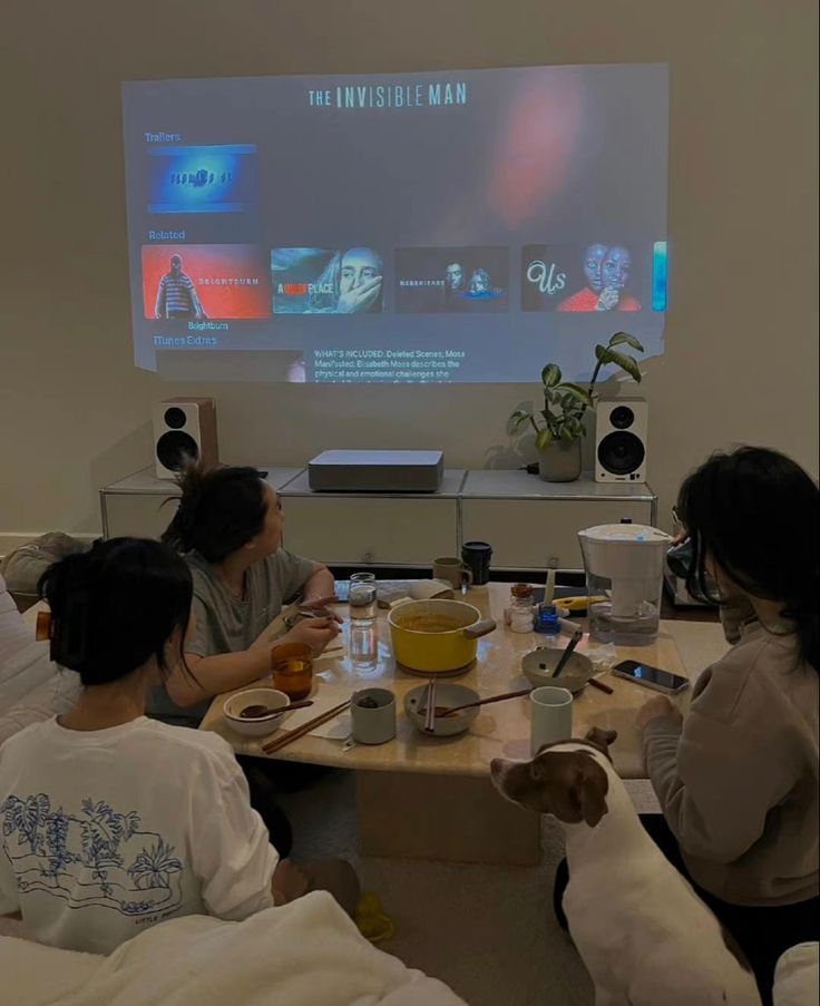 three people sitting at a table with food and drinks in front of a projector screen