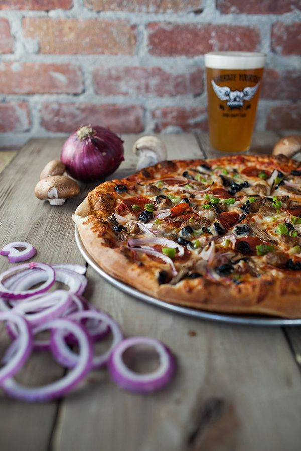 a pizza sitting on top of a metal pan next to onion rings and a beer