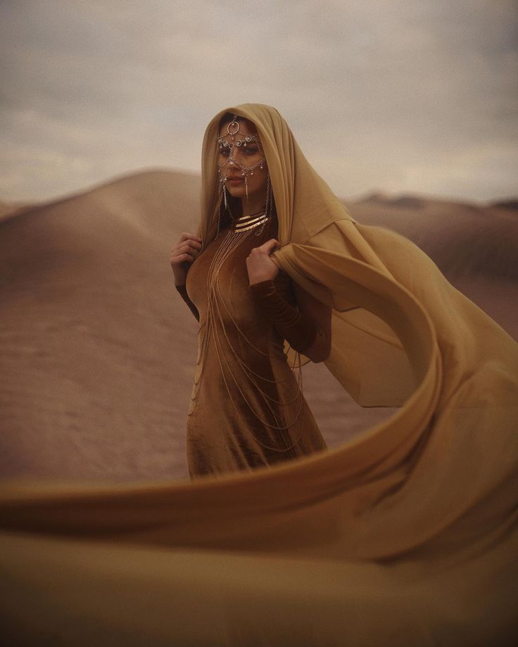 a woman standing in the desert holding a cell phone to her ear and wearing a veil