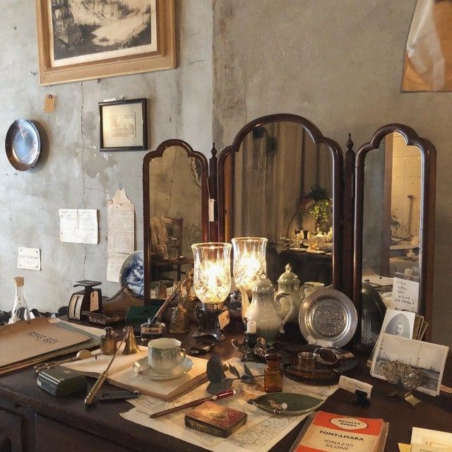 an old fashioned desk with antique items on it and other antiques in front of the mirror