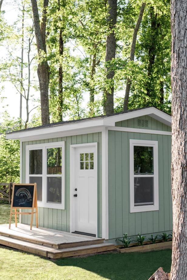 a small green and white shed sitting in the middle of a forest with a sign next to it