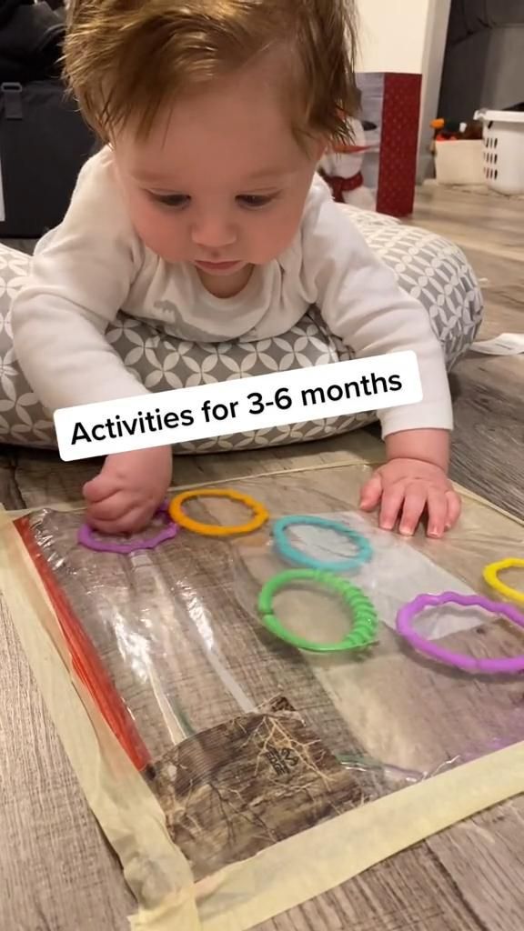 a baby playing with some scissors on the floor in front of a sign that says activities for 3 - 6 months