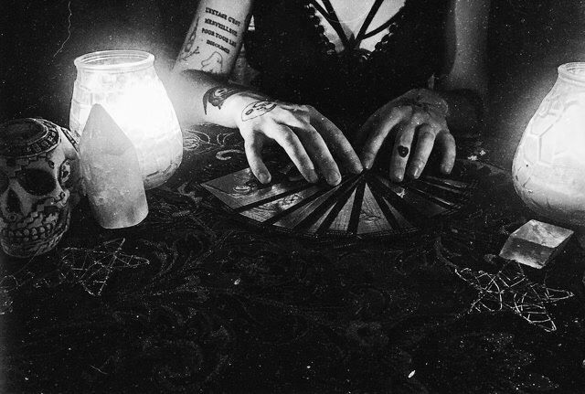 a woman sitting at a table with candles in front of her and two skulls around her