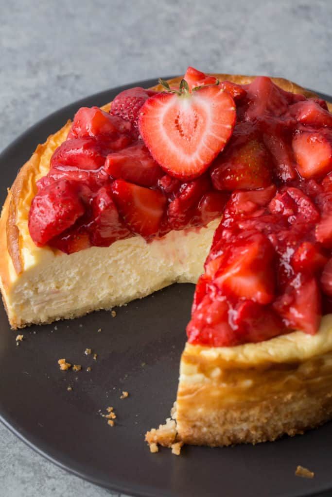 a strawberry cheesecake on a black plate with one slice cut out and the rest half eaten