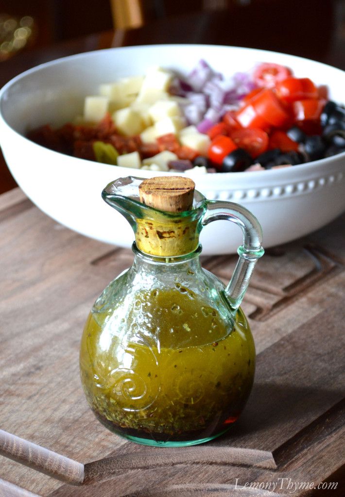 a glass bottle filled with green liquid sitting on top of a wooden cutting board next to a bowl of fruit