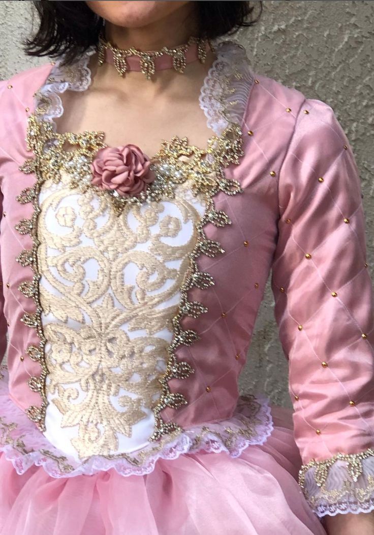 a woman wearing a pink and white dress with flowers on the chest, standing in front of a wall