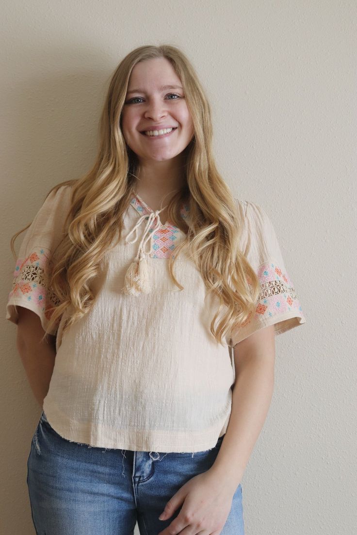 This cream top features an embroidered design on the neckline and sleeves, with tassel strings. This top is running oversized. Model is wearing a size SMALL. Model is 5 ft. 3 in. - 125ish lbs. Model typically wears small/medium in tops. Embroidered Cream Tops For Festival, Embroidered Cream Top For Festival, Spring Blouse With Short Sleeves And Tassel Ties, Casual Spring Peasant Top With Tassels, Casual Peasant Top With Tassels For Spring, Casual Short Sleeve Tops With Tassel Ties, Spring Cotton Peasant Top With Tassel Ties, Spring Blouse With Tassel Ties And Short Sleeves, Cotton Peasant Top With Tassel Ties For Spring